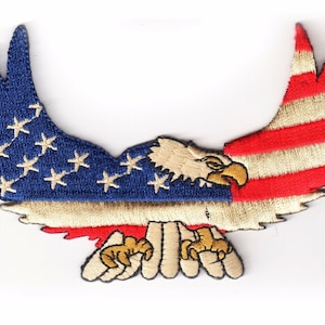 May include: An embroidered patch of a bald eagle with its wings spread, forming the shape of the American flag. The eagle is brown and white, with red and white stripes and blue stars on its wings.