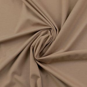 May include: A close-up of a smooth, light brown fabric with a soft, drapey texture. The fabric is folded and arranged in a way that shows its texture and drape.