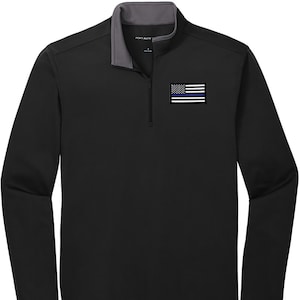 May include: Black long-sleeve shirt with a gray zipper and a small American flag with a blue line patch on the left chest. The shirt has a mock neck.