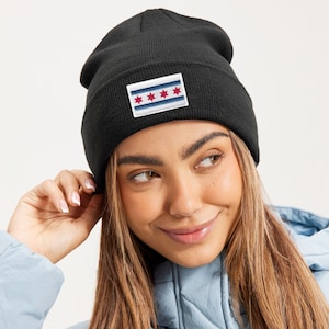 May include: Black beanie hat with a rectangular patch featuring the Chicago city flag. The patch has four red stars and two blue stripes on a white background. The hat is made of a soft, knitted material.