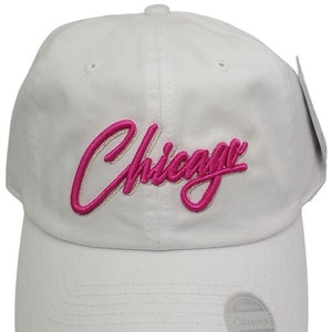 May include: White baseball cap with a pink embroidered "Chicago" logo. The cap has a white adjustable strap with a silver metal tag that reads "Everthing Classics Since 1984".