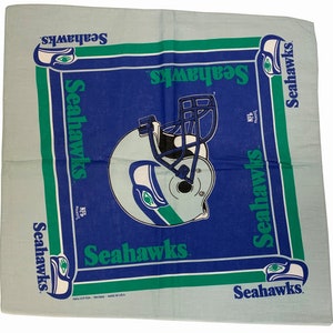 May include: A blue and green bandana with the Seattle Seahawks logo and the words "Seahawks" repeated multiple times. The bandana is made of 100% cotton and is printed in the USA.