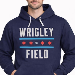 May include: Navy blue hoodie with the text "WRIGLEY FIELD" in white block letters. The design includes red stars and blue stripes, with "BUILT 1914" in the center. The hoodie has a drawstring hood and a front pocket.