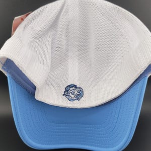 May include: A white and light blue baseball cap with a mesh back. The front of the cap features a blue and white embroidered logo of a cartoon creature with the text "UNC" above it.