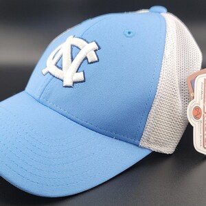 May include: A light blue baseball cap with a white mesh back. The cap features a white embroidered logo of the letters "UNC" in a stylized font.