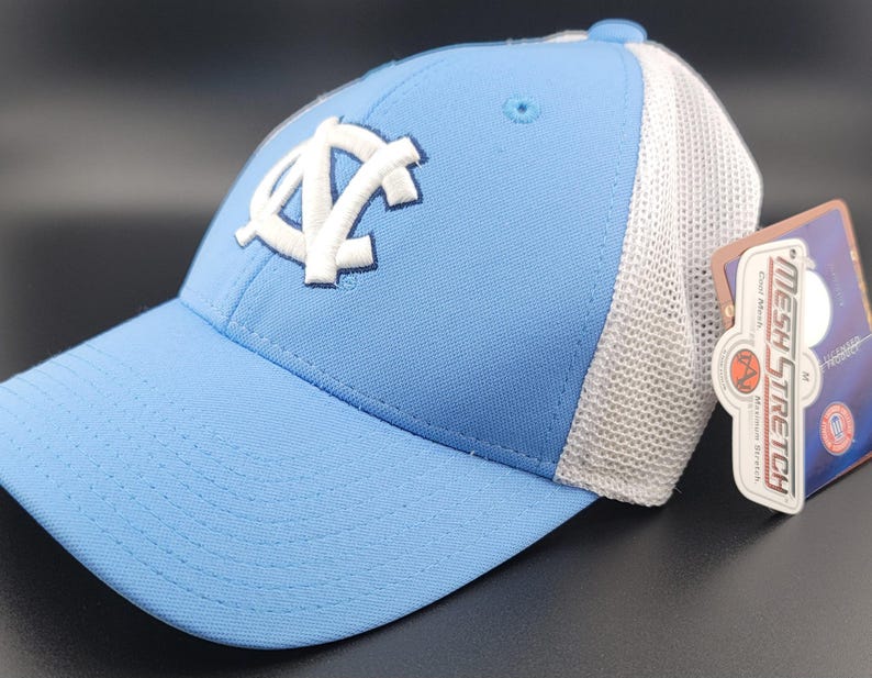 May include: A light blue baseball cap with a white mesh back. The cap features a white embroidered logo of the letters "UNC" in a stylized font.