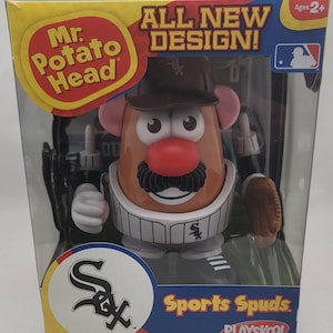 May include: A Mr. Potato Head Sports Spuds toy in a box. The toy is dressed as a Chicago White Sox baseball player. The box has the words "All New Design!" and "Sports Spuds" on it. The box is blue, yellow, and red. The toy is brown, white, and black.