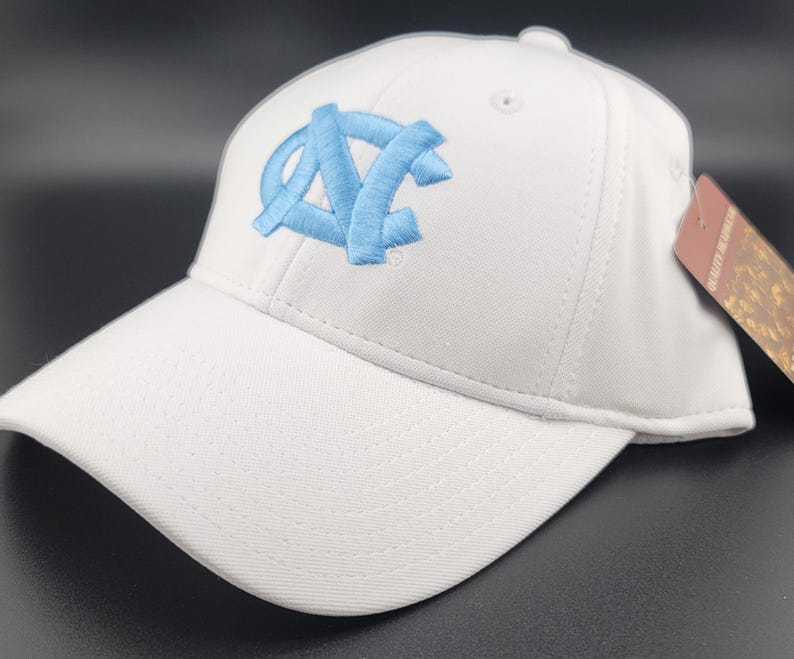 May include: White baseball cap with a curved brim. The cap features a light blue embroidered logo on the front. A tag is attached to the side. The cap is made of a textured fabric.