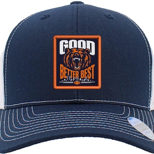 May include: Navy blue and white trucker hat with a stitched brim. The front panel features a rectangular patch with a bear graphic and the words "GOOD BETTER BEST". A stylish accessory for sports fans.
