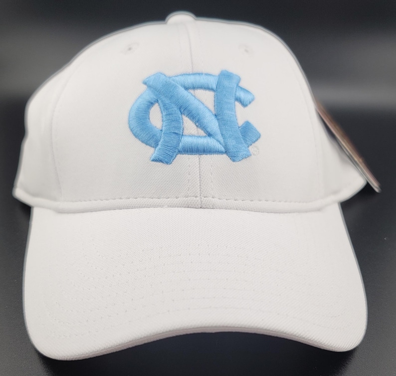 May include: White baseball cap with a light blue embroidered logo. The cap features a curved brim and a structured crown. The logo is a stylized interlocking "NC" design.
