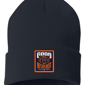 May include: Navy blue beanie with a rectangular patch featuring a roaring bear graphic. The patch has the words "GOOD BETTER BEST" in white and orange. The beanie is a winter accessory.