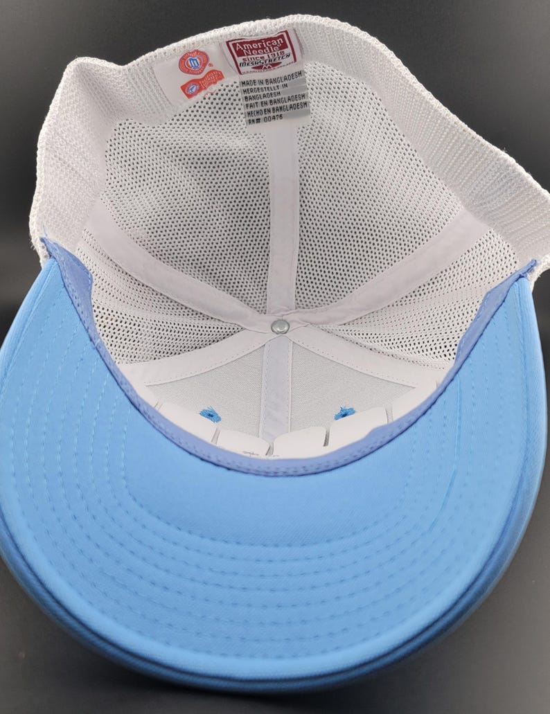 May include: The inside of a white and light blue baseball cap. The cap is made of mesh and has a white label that reads "American Needle" and "Made in Bangladesh".