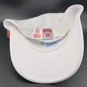 May include: A white baseball cap with a curved brim, featuring a light blue embroidered design on the underside. The cap has a tag that reads "American Needle since 1918 TECH/STRETCH".
