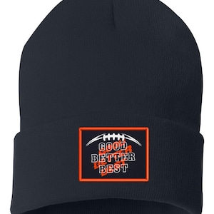 May include: A navy blue beanie hat with a rectangular patch featuring the words "GOOD BETTER BEST" in white and orange, with a football graphic. The hat is made of a soft, knitted material.