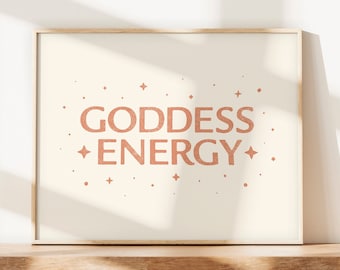 May include: A framed print with a white background and the text "GODDESS ENERGY" in a peachy-pink color. The text is surrounded by small stars and dots.