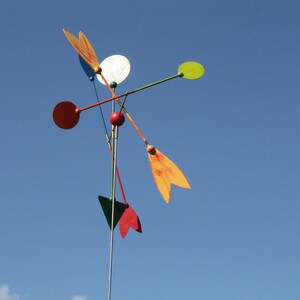 May include: A colorful mobile with red, orange, yellow, green, and white circular and teardrop-shaped pieces. The mobile is suspended from a metal rod.