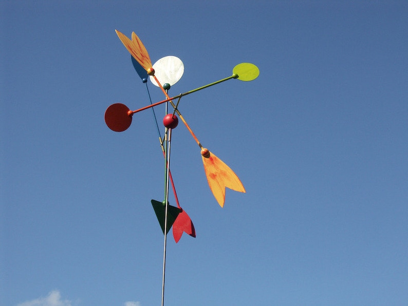 May include: A colorful mobile with red, orange, yellow, green, and white circular and teardrop-shaped pieces. The mobile is suspended from a metal rod.