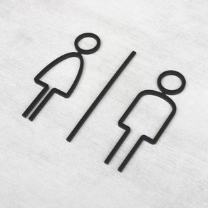 Puede incluir: Esquema en blanco y negro de un s&iacute;mbolo de ba&ntilde;o masculino y femenino sobre un fondo blanco.