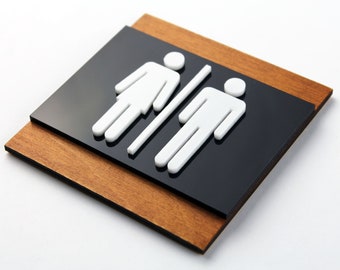 May include: A black and brown wooden sign with white raised symbols for a restroom. The symbols are a stylized female figure on the left and a stylized male figure on the right.