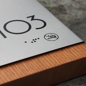 May include: A silver metal sign with the number 103 and a no smoking symbol. The sign is mounted on a wooden base.