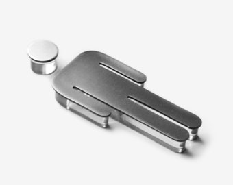 May include: A silver metal cutout of a person with a round head. The cutout is lying on a white surface.