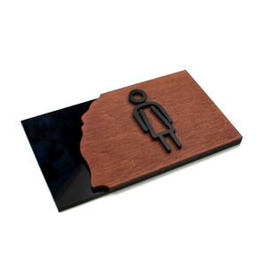 May include: A black and brown sign with a stylized female figure icon. The sign is made of wood and acrylic.