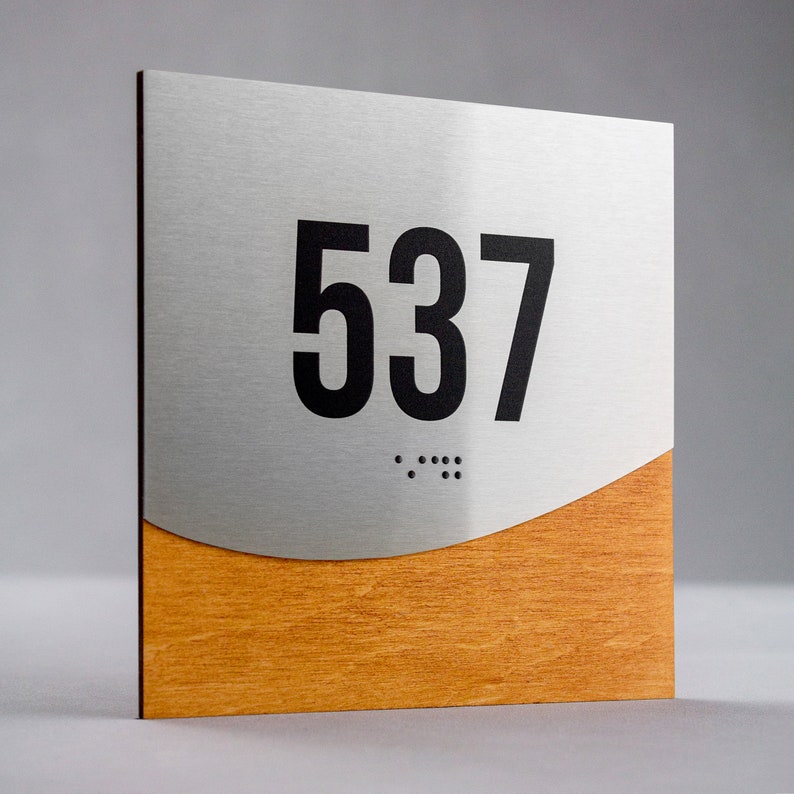 May include: A silver and wood room number sign with the number 537 in black lettering and braille dots below.