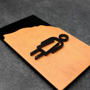 May include: A black and brown wooden sign with a black silhouette of a person in a dress. The sign is for a restroom.