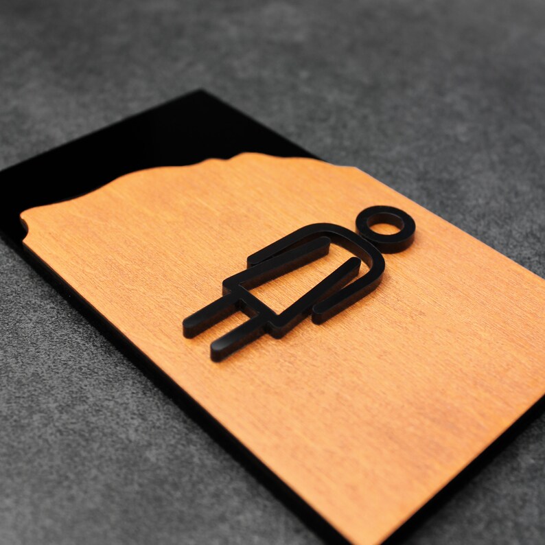 May include: A black and brown wooden sign with a black silhouette of a person in a dress. The sign is for a restroom.
