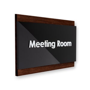 May include: A dark brown wooden sign with a black acrylic panel that says "Meeting Room" in white raised letters.