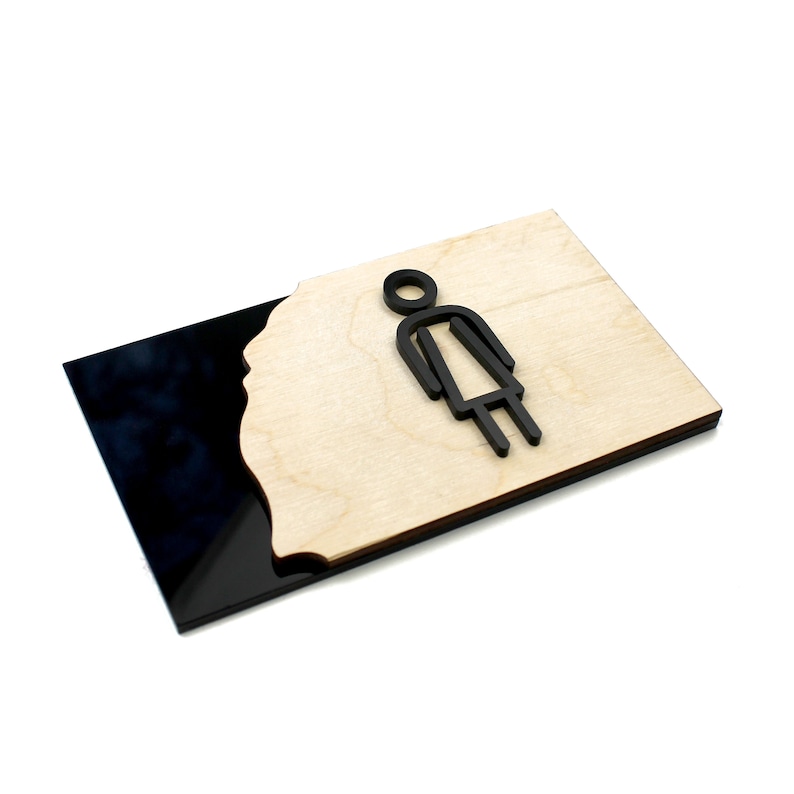 May include: A black and wood sign with a stylized female figure icon. The sign is made of two layers, a black acrylic base and a wood top layer with a cut-out shape.