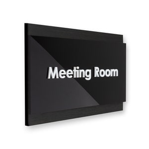 May include: Black sign with a white, raised "Meeting Room" label. The sign has a wood frame.
