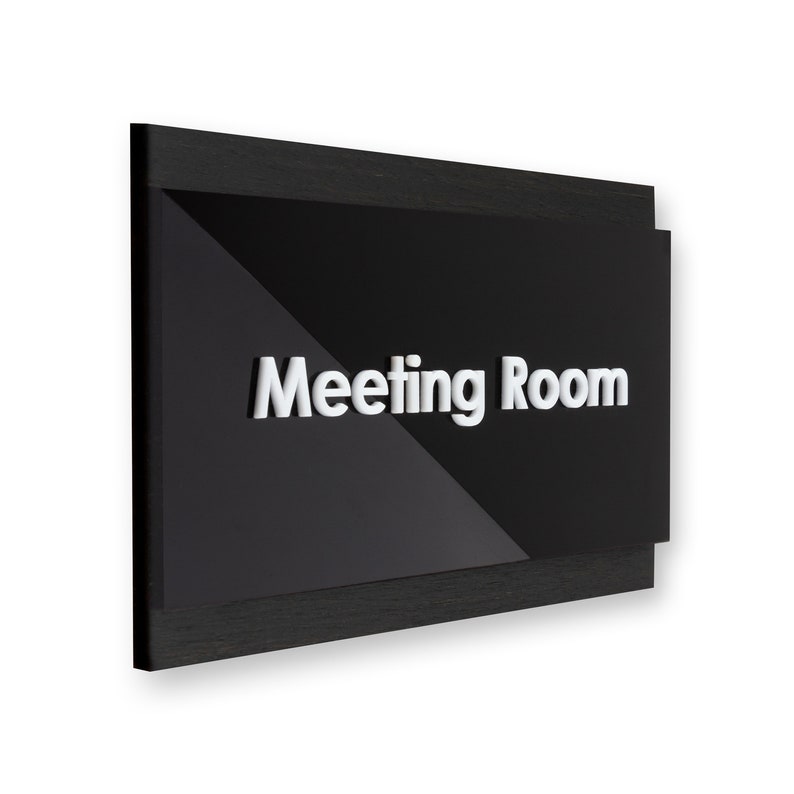 May include: Black sign with a white, raised "Meeting Room" label. The sign has a wood frame.