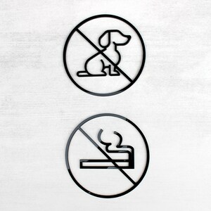 May include: Two black and white signs with a diagonal line through them. The top sign has a silhouette of a dog and the bottom sign has a silhouette of a cigarette.