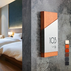 May include: A wooden and metal room number sign with the number 103 on a gray wall. The sign has a wood frame and a silver metal insert with the number and a no smoking symbol.