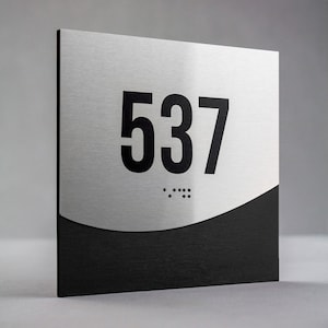 May include: A silver and black room number sign with the number 537 in black lettering. The sign has braille dots below the number.