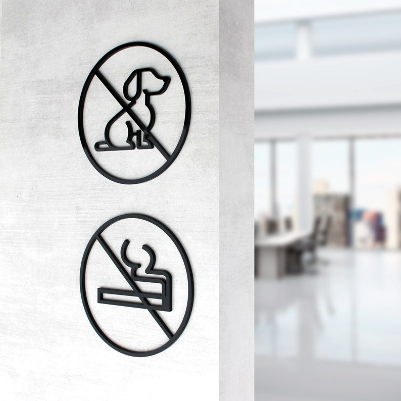 May include: Two black and white signs with a diagonal line through them. The top sign shows a dog silhouette and the bottom sign shows a cigarette silhouette. Both signs are on a white wall.