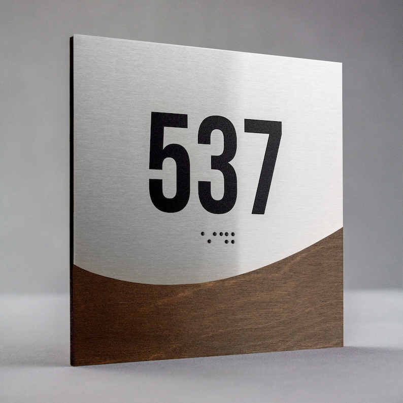 May include: A silver and brown room number sign with the number 537 in black lettering and braille dots below.