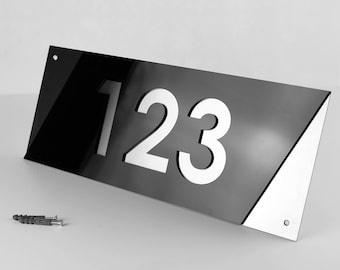 Puede incluir: Placa de número de casa moderna en blanco y negro con el número 123 recortado. La placa tiene un borde biselado y está hecha de metal.