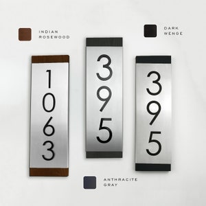 May include: Three silver house number plaques with black numbers. The numbers are 1063, 395, and 395. The plaques have different colored frames: Indian Rosewood, Dark Wenge, and Anthracite Gray.