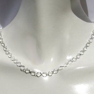 May include: A silver chain necklace on a white mannequin bust.