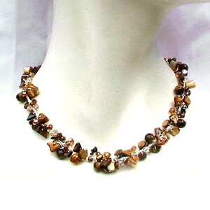 Peut inclure: Un collier en pierre de œil de tigre brun et or avec des perles de verre transparentes. Le collier est sur un mannequin blanc.