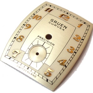 Puede incluir: Una esfera de reloj de color dorado con marcas negras y números dorados. La esfera del reloj dice "Gruen Curvex Precision" y "Switzerland".