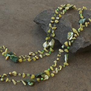 May include: A multi-strand necklace made of green and yellow stones and beads. The necklace is draped over a dark grey rock.