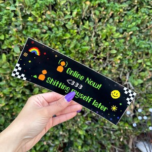 May include: Black sticker with pixelated graphics and text. The design includes a rainbow, smiley face, and the phrases "Online Now!" and "Shitting myself later." The sticker has a checkered border.