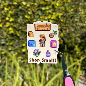 Puede incluir: Una pegatina blanca con gráficos pixelados y el texto "Pierre's" en la parte superior. La pegatina presenta varios iconos, incluyendo un personaje, un cofre, una bolsa de monedas, un cubo azul, un ramo de flores moradas, una botella morada y las palabras "Shop Small!"