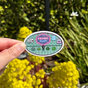 Puede incluir: Una pegatina ovalada con un diseño pixelado. La pegatina presenta el texto "KROBUS fresh" en un letrero rosa neón. Debajo del letrero hay plantas pixeladas y un personaje. La pegatina también incluye el texto "100% VOID FREE".