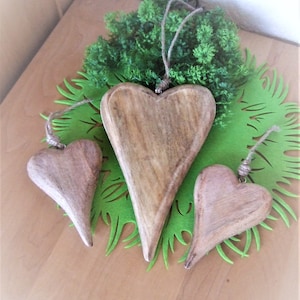 May include: Three wooden heart-shaped ornaments hanging from twine. The hearts are different sizes and are arranged on a green felt background.