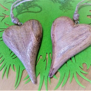 May include: Two wooden heart-shaped ornaments with a rustic brown finish, hanging from twine strings. The hearts are displayed on a green background.