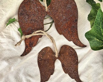 May include: Two decorative angel wing ornaments crafted from rusted metal with a textured, weathered brown finish. Each pair of wings features a hole at the top, threaded with a natural jute twine cord for hanging, showcasing a rustic aesthetic.